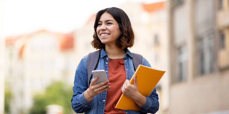 estudante na faculdade com celular na mão carregando caderno laranja