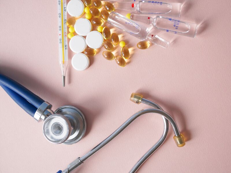 Estetoscópio e medicamentos sobre superfície rosa