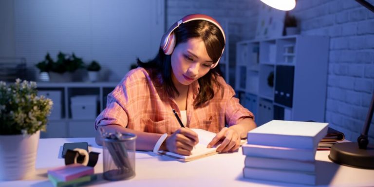 Estudante escrevendo com fones de ouvido à noite