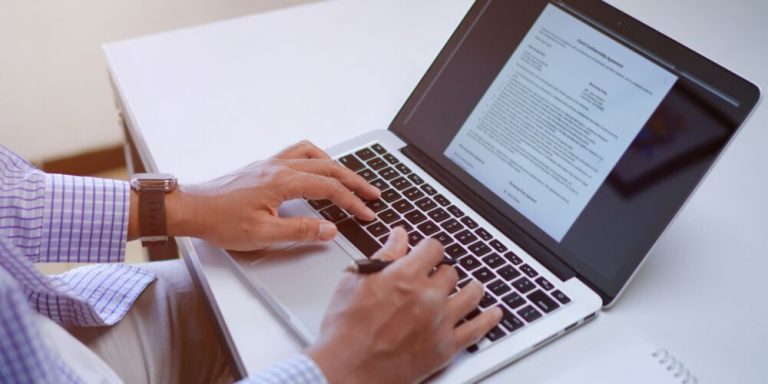 Pessoa digitando em laptop com documento visível