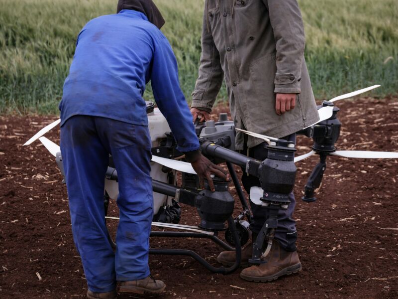 Homens ajustando um drone em campo agrícola