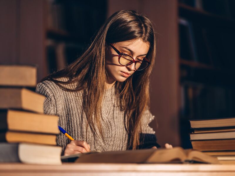 Jovem estudando em biblioteca com livros ao redor